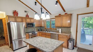 Una cocina con encimeras de granito, electrodomésticos de acero inoxidable, armarios de madera y una isla grande con taburetes de bar.