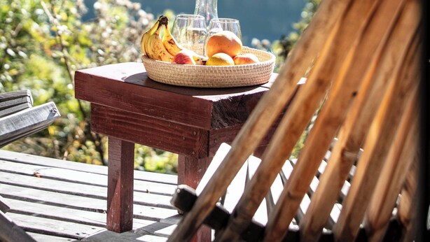 A wooden table with a fruit basket and a vase, set against a mountainous backdrop. - Hermoso Eco Lodge (San Martín de los Andes)
