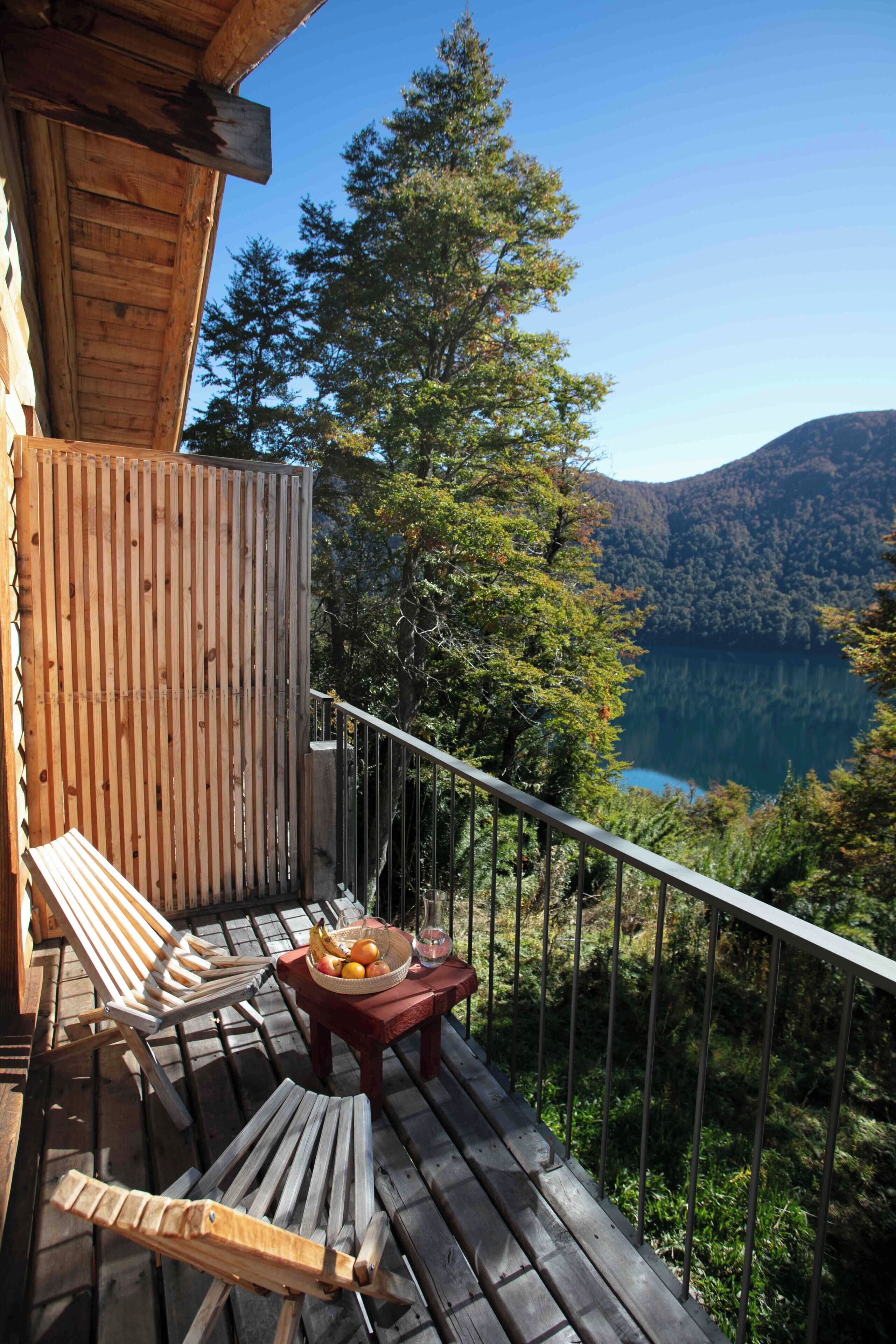 A wooden deck with a table and chairs, overlooking a lake and forested hills.