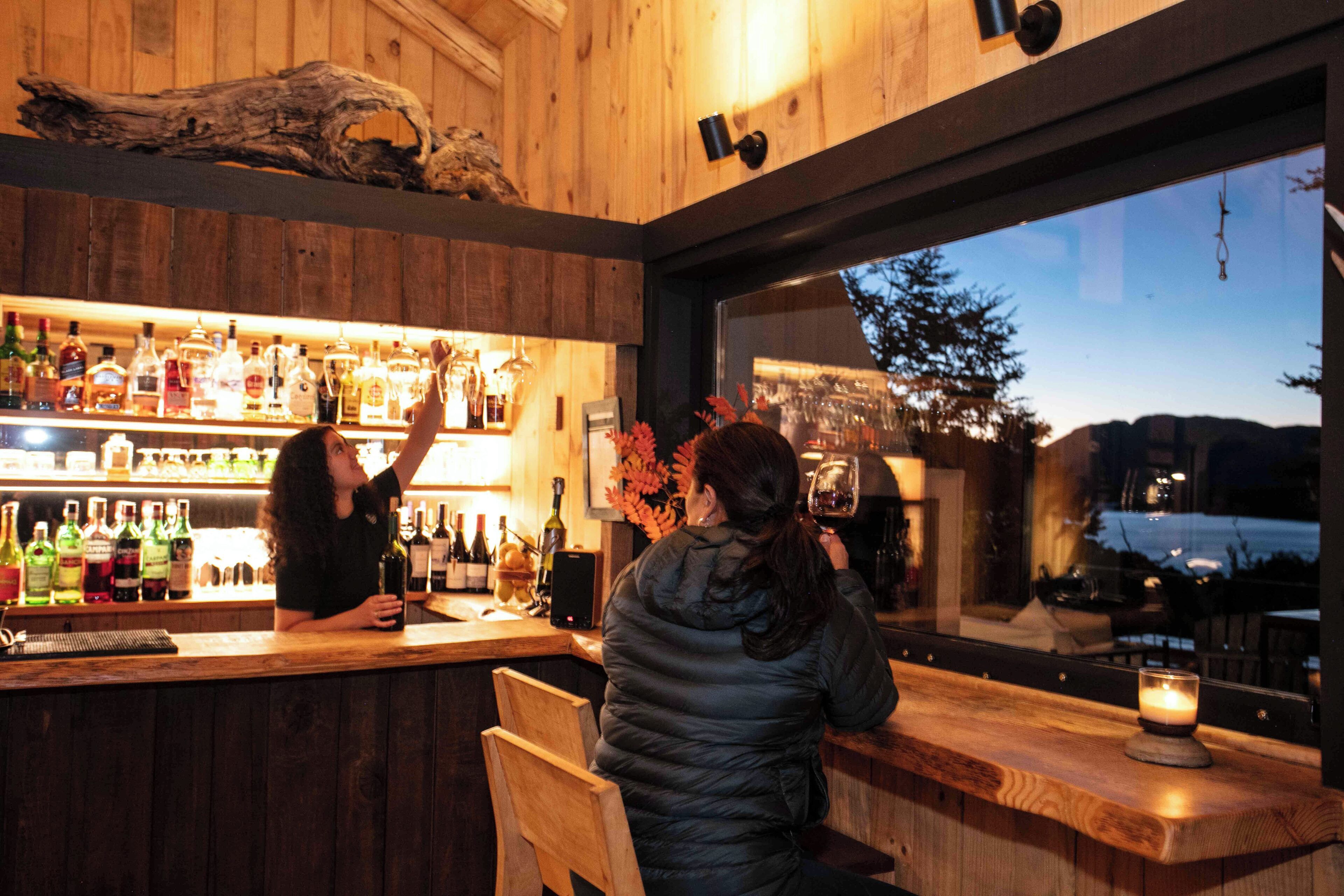 Un espace bar avec des murs en bois, une grande fenêtre et diverses bouteilles d’alcool.