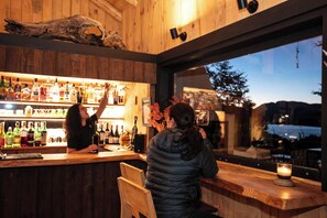 A bar area with wooden walls, a large window, and various bottles of alcohol. - Hermoso Eco Lodge (San Martín de los Andes)