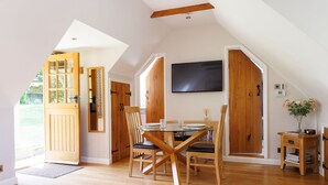 Un comedor con una mesa y sillas de madera, un televisor montado en la pared y una puerta de madera que da al exterior.