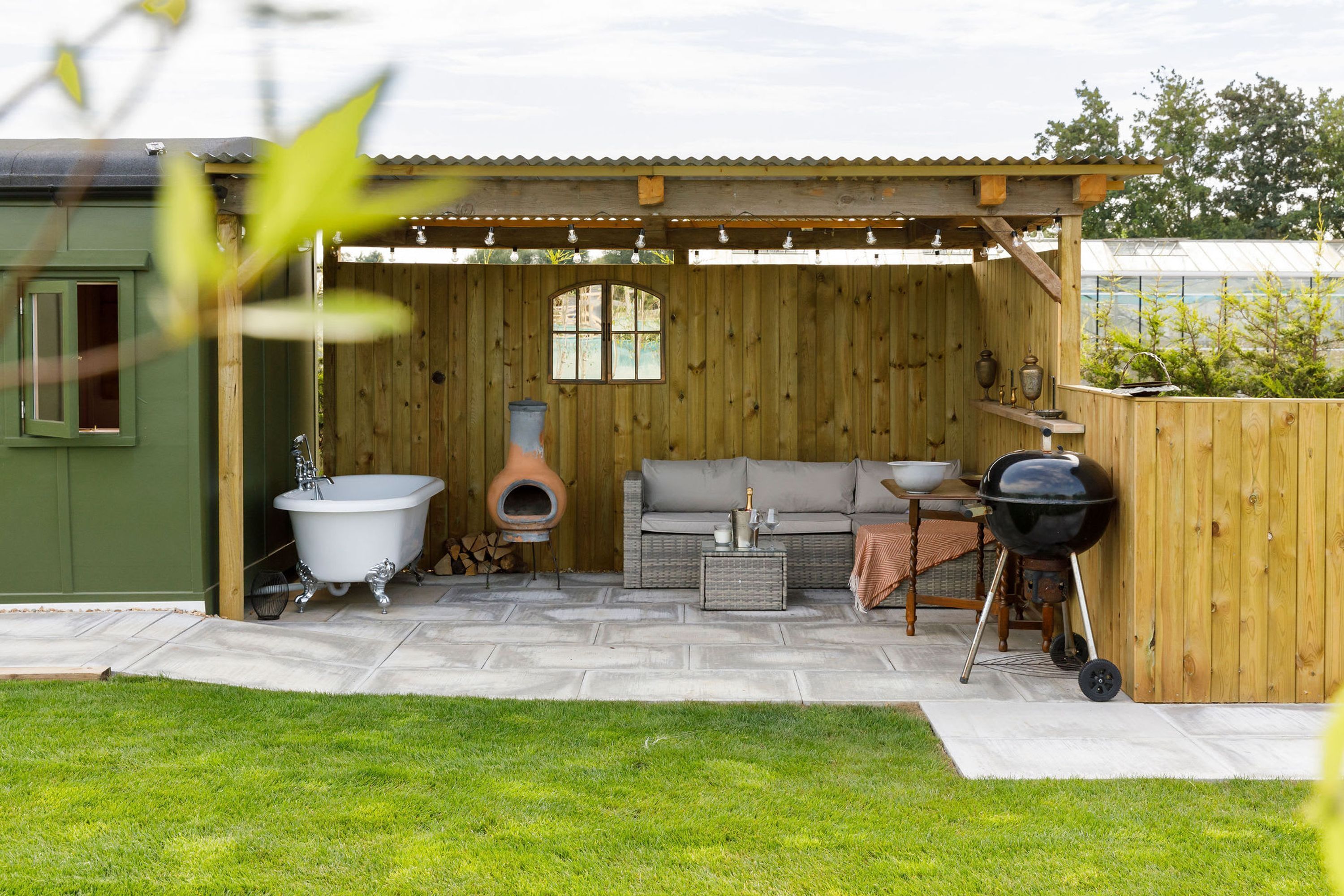 A wooden outdoor patio with a built-in barbecue, a vintage clawfoot bathtub, and a cozy seating area.