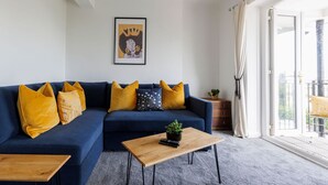 A living room with a blue sofa, yellow cushions, a wooden coffee table, and a framed picture on the wall. - Two bed Apartment With Sea Views in Bognor Regis (Bognor Regis)