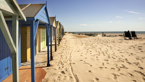 A row of beach huts with wooden floors and blue walls, leading to a sandy beach with footprints. - Two bed Apartment With Sea Views in Bognor Regis (Bognor Regis)