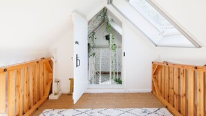 A room with a sloped ceiling, wooden railings, a white door with a 'b' sign, and a view of a staircase with greenery. - Enchanting 4BD Cottage Lodge Nr Eartham Wood (Petworth)