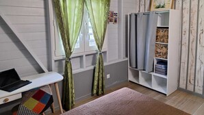 Una habitación con una cama, un escritorio con una computadora portátil, una estantería y cortinas verdes.