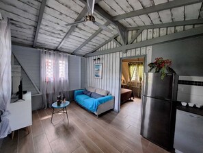 A cozy room with a blue sofa, a small round table, a refrigerator, and a kitchen area. - "Kaz Ixora" Bungalow (Les Anses-d'Arlet)