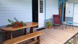 Una terraza de madera cubierta con una mesa de picnic y bancos, una silla roja y una pequeña mesa azul.