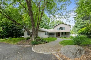 A two-story house with a front porch, a driveway, and surrounding greenery.