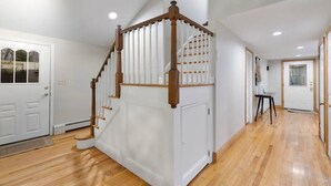 A spacious hallway with wooden flooring, a white door, and a staircase with wooden railings.