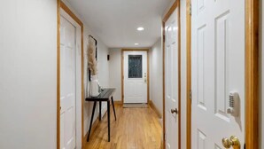 A hallway with wooden flooring, white doors, and a small table with a vase.