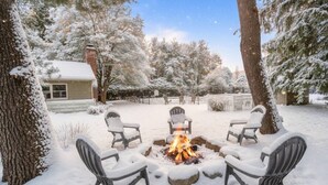 A snow-covered outdoor seating area with a fire pit surrounded by chairs.