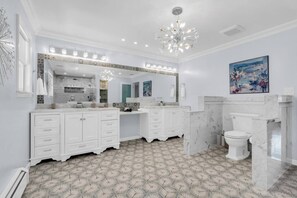 A spacious bathroom with a large mirror, white cabinetry, a marble floor, and a chandelier.