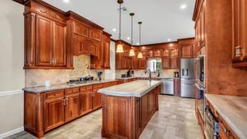 A spacious kitchen with wooden cabinetry, a large island, stainless steel appliances, and pendant lighting.