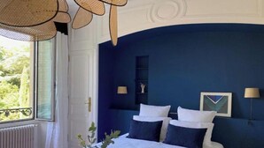 Un dormitorio con una cama grande, dos lámparas de noche, una ventana con vistas a zonas verdes y una pared de acento azul.