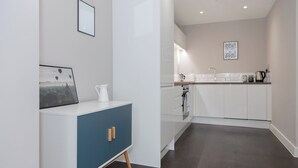 Une cuisine moderne avec des meubles blancs, un meuble d’accent bleu et une machine à café posée sur le plan de travail.