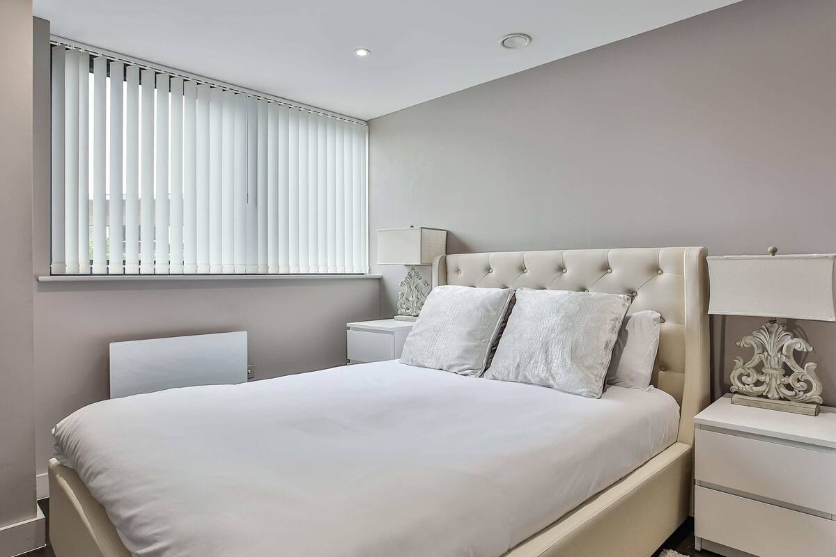 Une chambre à coucher avec un grand lit, deux tables de chevet et une fenêtre avec des stores.