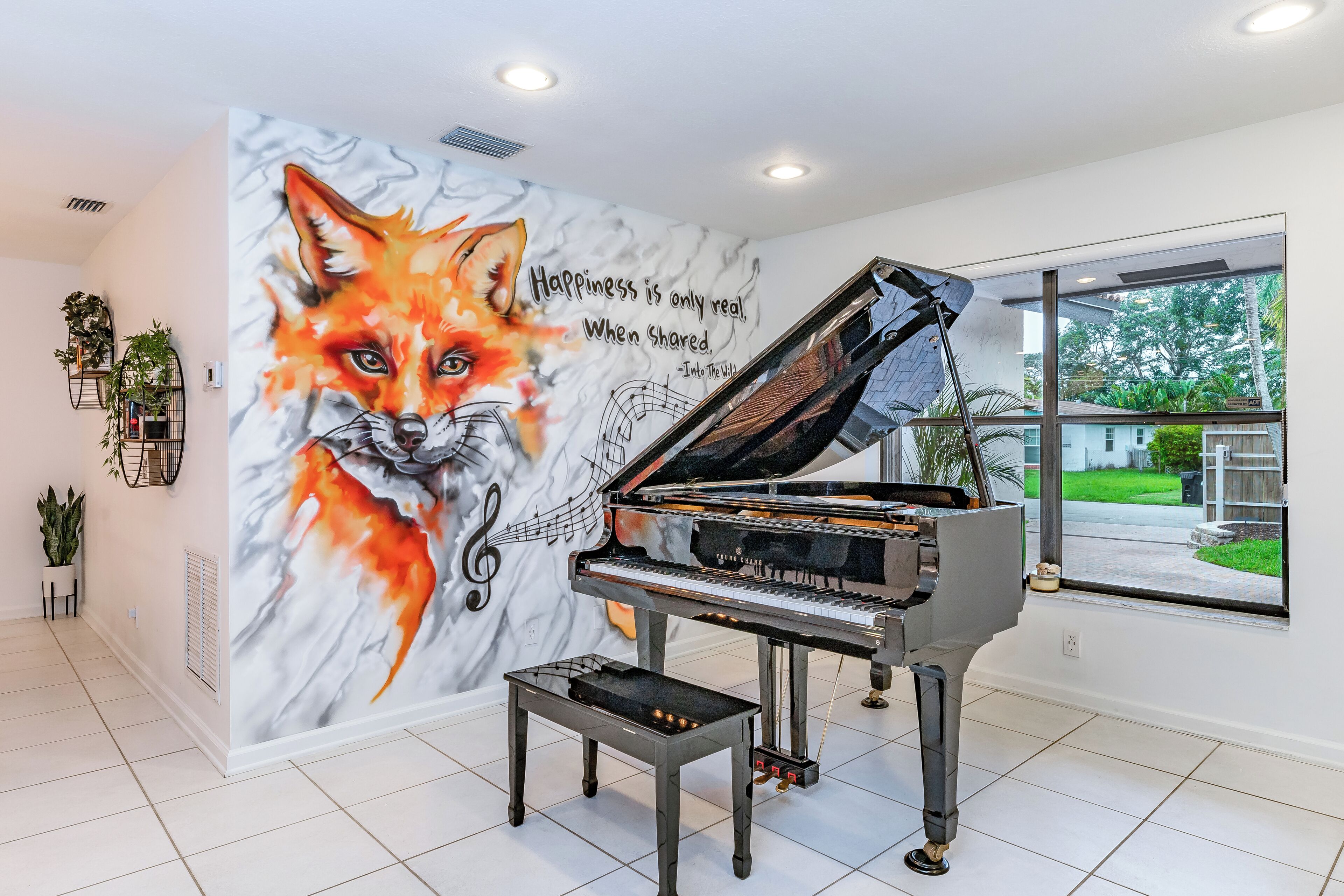 A grand piano in a well-lit room with a mural of a fox and a quote on the wall.