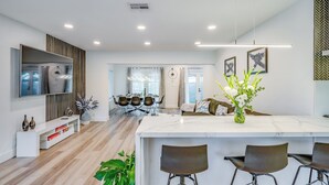 Una cocina moderna con una isla de mármol, taburetes de bar y una zona de comedor con mesa y sillas.