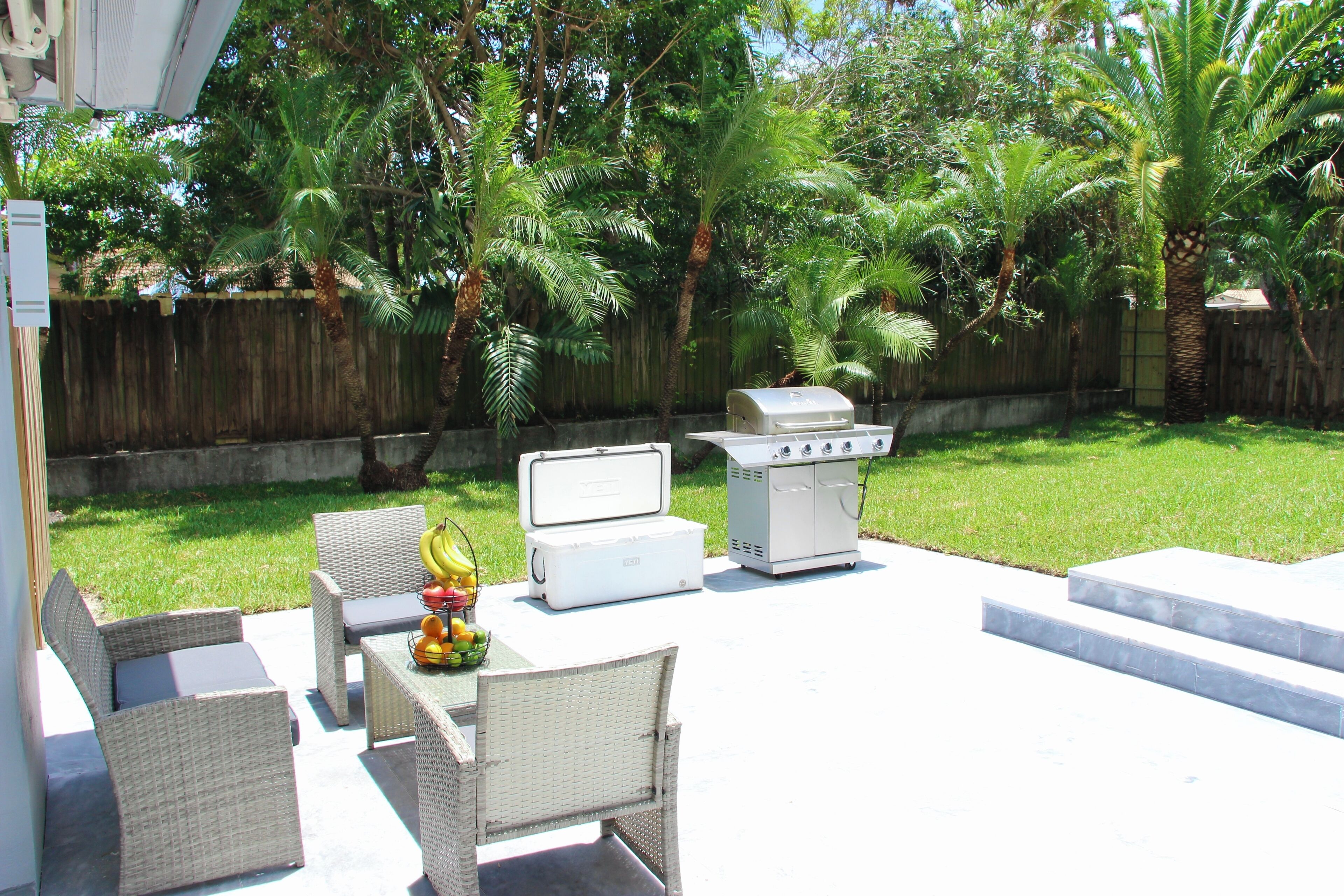 An outdoor patio with wicker furniture, a grill, and a cooler.