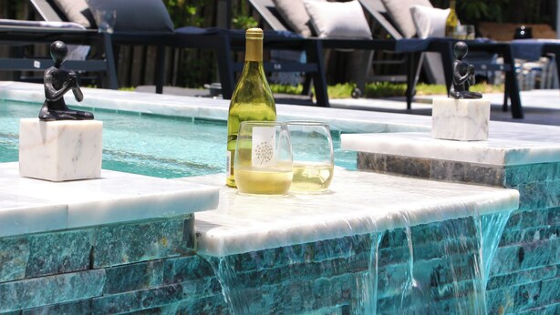 Un área junto a la piscina con sillones de descanso, un borde de mármol, una botella de vino y dos copas.
