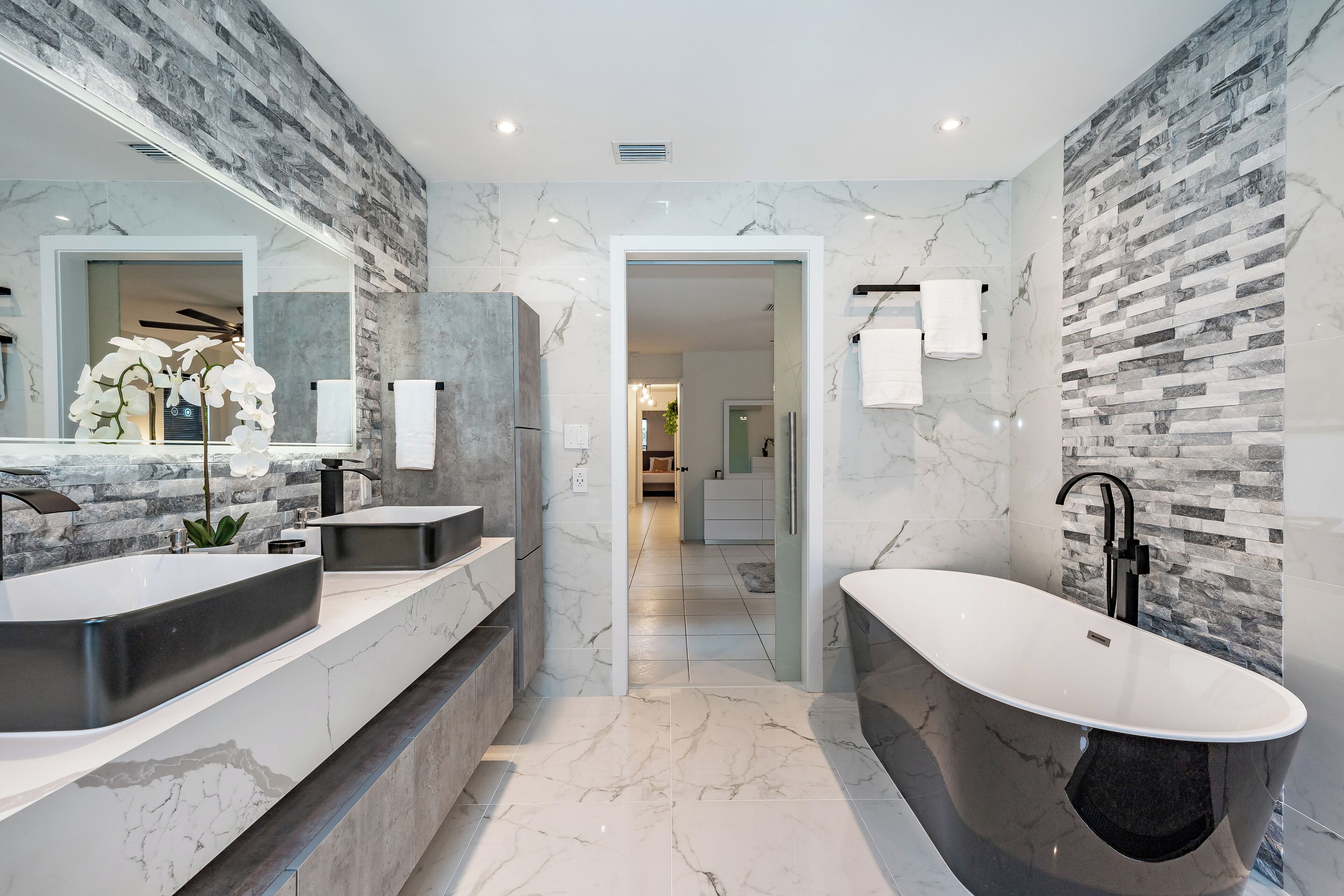 Un baño moderno con encimeras de mármol, una bañera independiente y un espejo grande.
