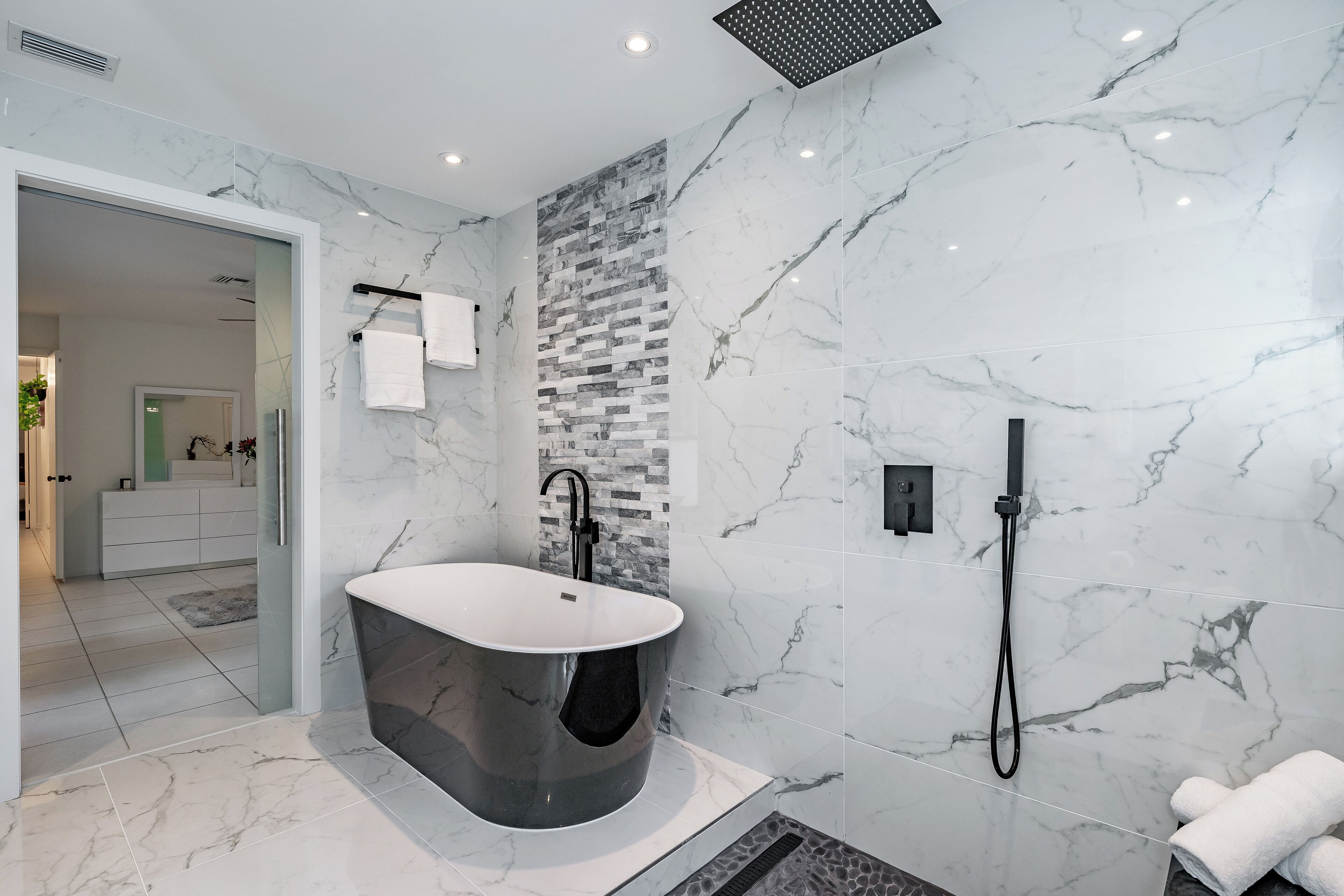 A modern bathroom with a freestanding bathtub, a shower, and a tiled wall with a mosaic pattern.