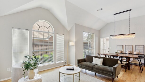 A spacious living area with a high ceiling, large windows, a dining table, and a modern chandelier. - Family Fun Retreat: Pool & Entertainment Haven! 4 Bedroom Home by RedAwning (Frisco)