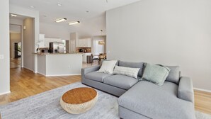 A modern living room with a grey sectional sofa, a round wooden coffee table, and a ceiling fan. - Family Fun Retreat: Pool & Entertainment Haven! 4 Bedroom Home by RedAwning (Frisco)