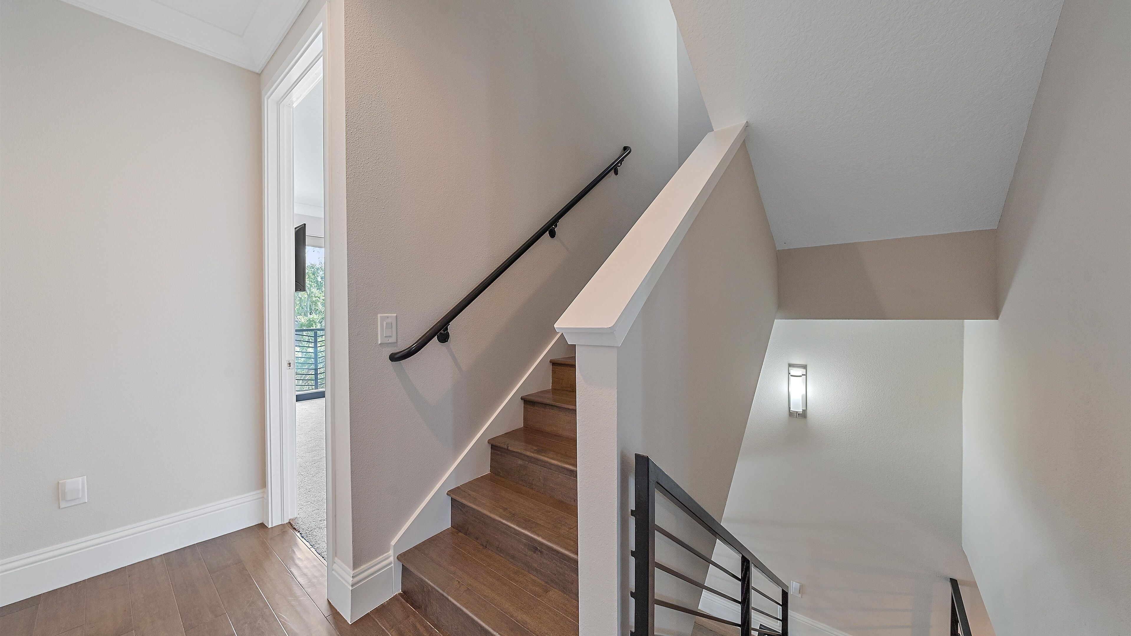 A staircase with wooden steps and a black handrail, leading to a landing with a white railing.
