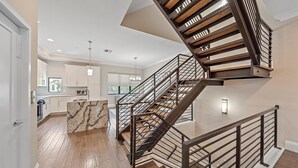 A spacious kitchen with white cabinets, a marble island, and a modern staircase with wooden steps and metal railings. - Cityscape Retreat 2 Bedroom Townhouse by RedAwning (Sarasota)