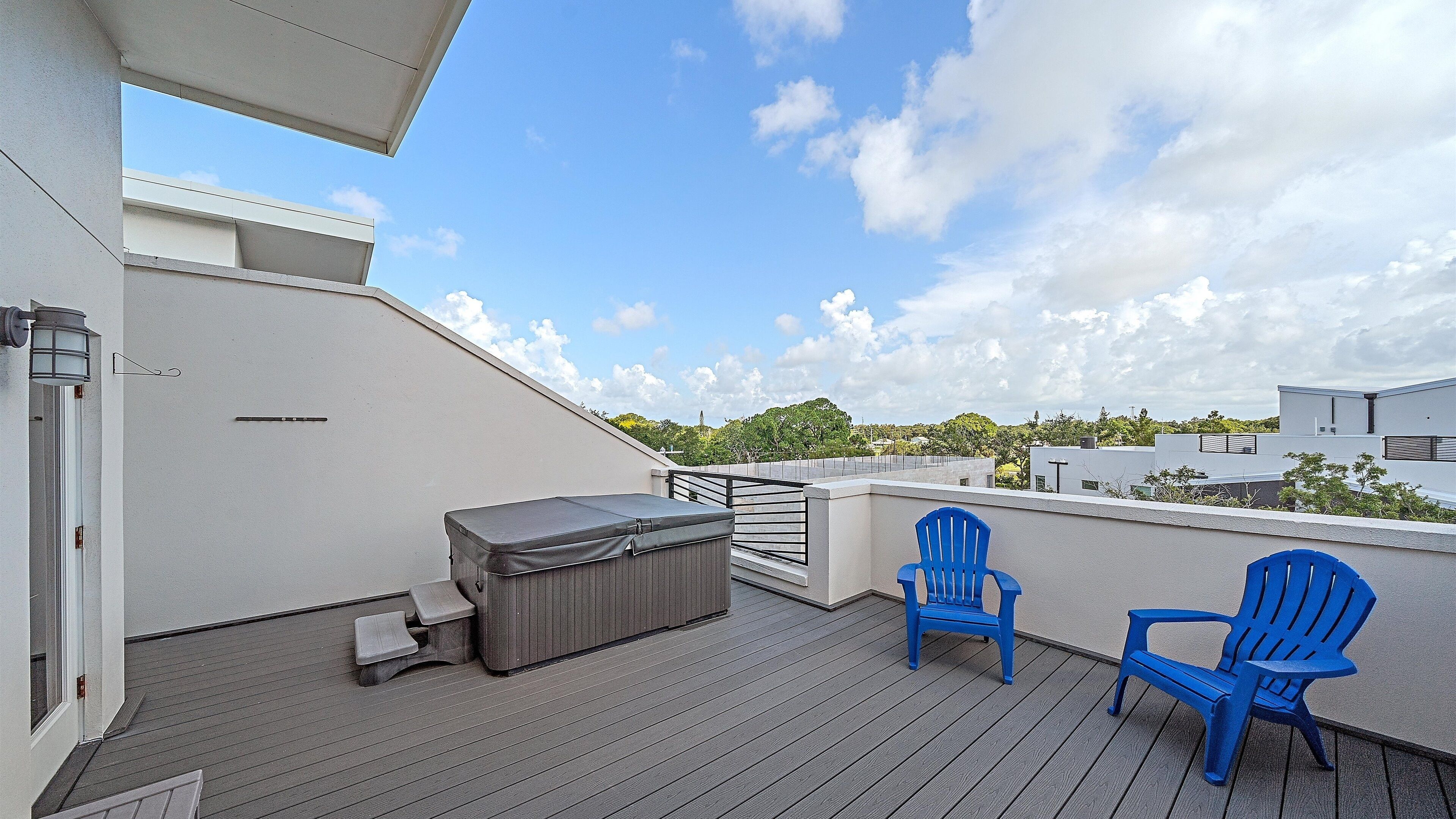 A rooftop deck with a barbecue grill, two blue chairs, and a small table.