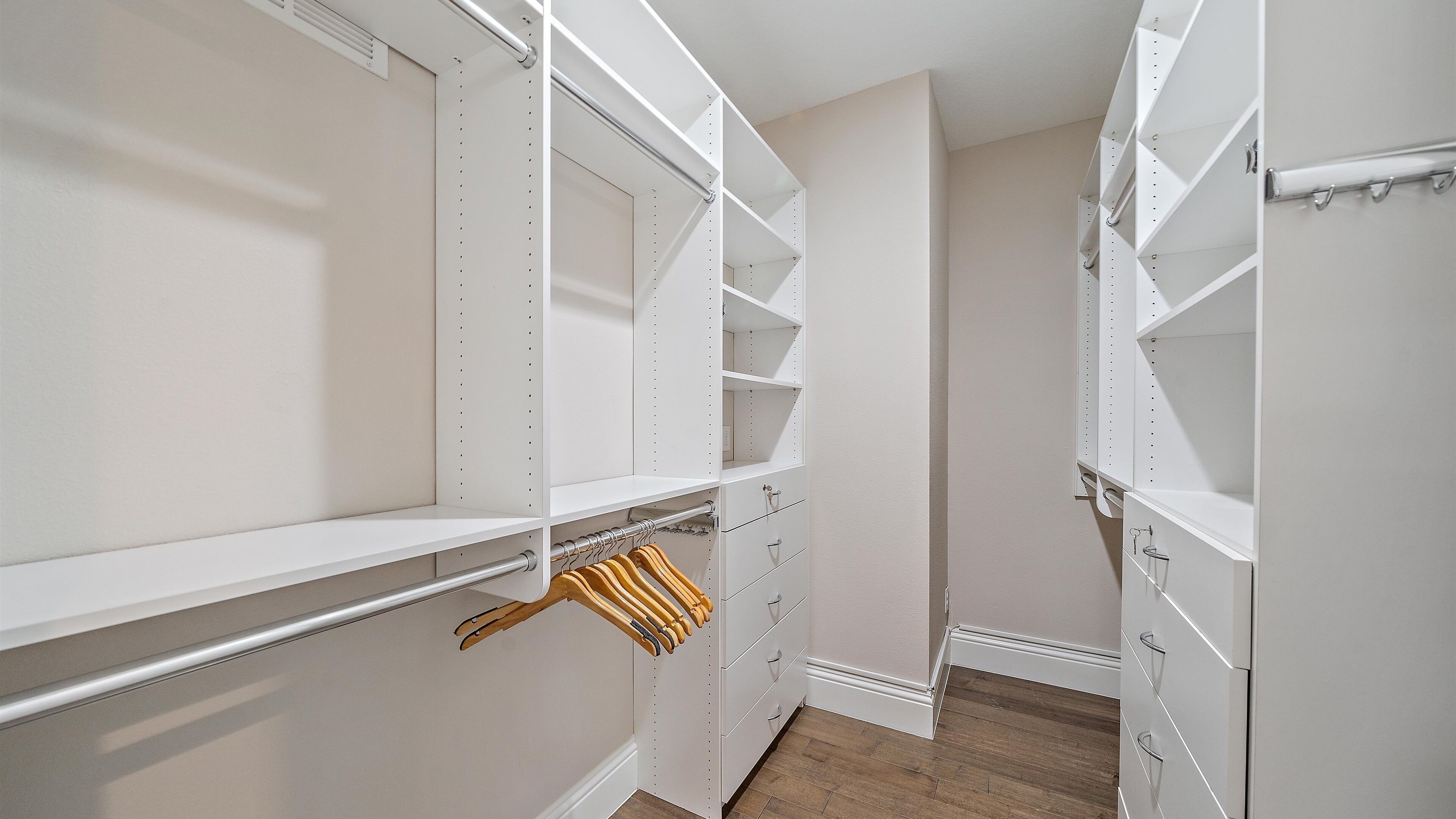 Un vestidor con estanterías blancas, perchas de madera y suelo de madera.