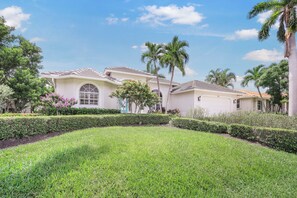 A large, single-story house with a well-maintained lawn and palm trees.