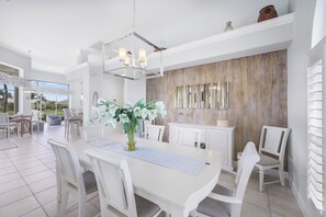 A spacious dining area with a white table and chairs, a chandelier, and a view of the outdoors.