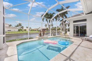 An indoor swimming pool with clear views of a river and palm trees, surrounded by a covered patio area. - W Exposure Waterfront Home | Pool & Dock (Marco Island)