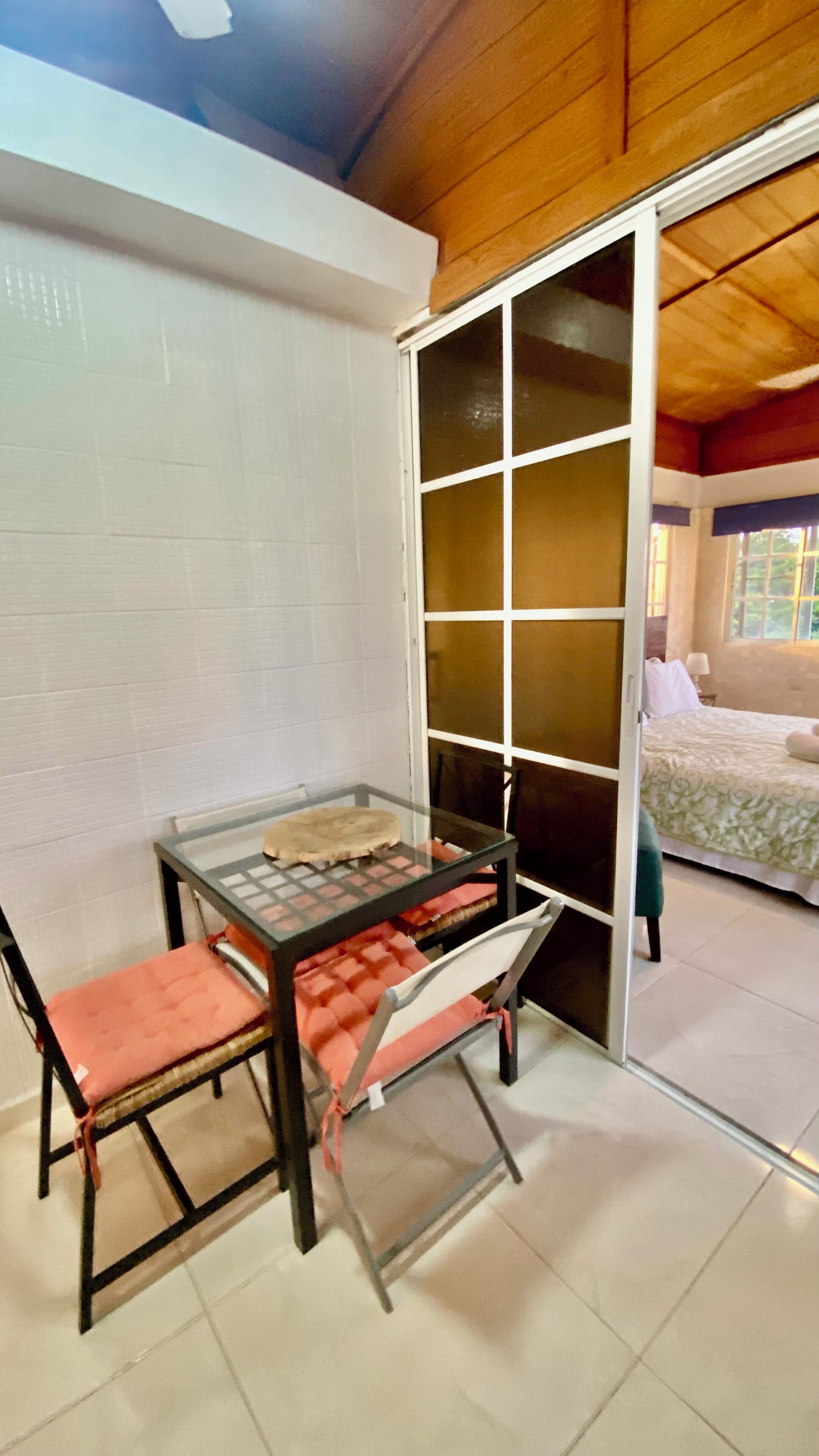 A room with a glass-top table, two chairs, a sliding glass door leading to a bedroom, and a tiled floor.