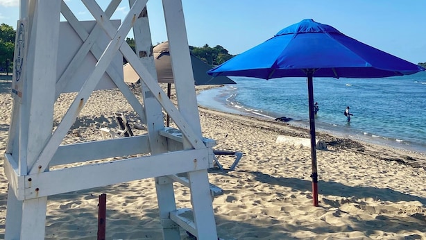 A lifeguard tower and a blue umbrella on a sandy beach.