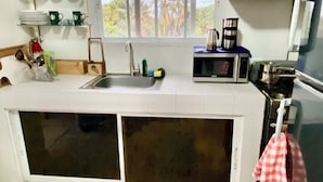 A compact kitchen with a window, a sink, a microwave, and a stove.