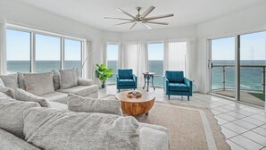 A spacious living room with a large sofa, two armchairs, a coffee table, and a ceiling fan. Large windows offer a view of the ocean. - Beautiful 3 Bed, 2 Bath Gulf Front Condo/Free Platinum Beach Service! (Pensacola Beach)