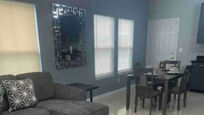 A modern living room with a sectional sofa, a coffee table, and a dining area with a table and chairs. -  2BR Elegant Apartment for 8, Edinburg Texas (Edinburg)