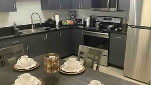 A modern kitchen with dark cabinets, stainless steel appliances, and a dining table set with white plates and napkins. -  2BR Elegant Apartment for 8, Edinburg Texas (Edinburg)