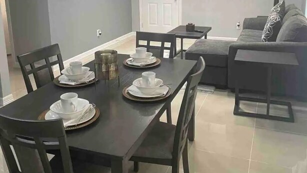 A dining area with a table set for four, a sofa, a TV, and a door. -  2BR Elegant Apartment for 8, Edinburg Texas (Edinburg)