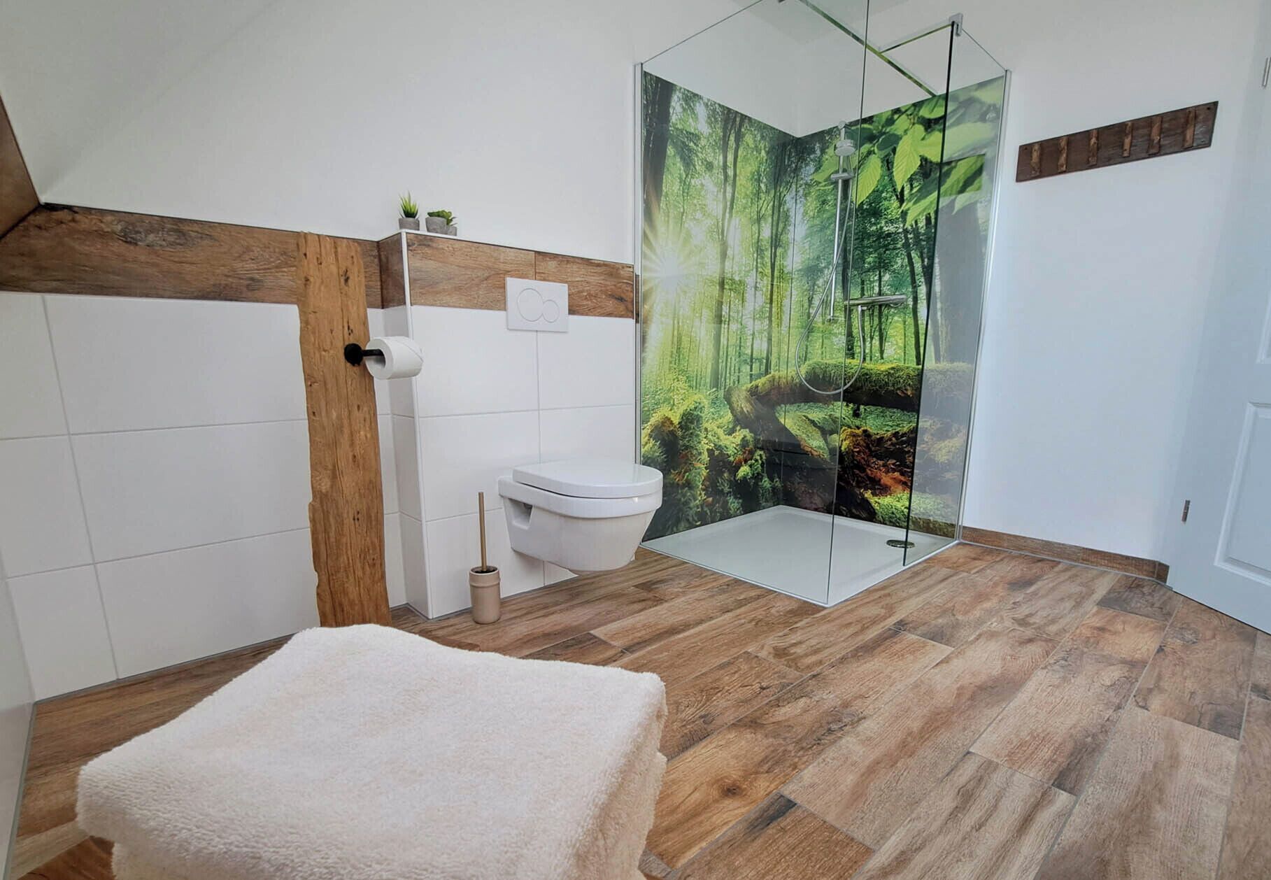 A modern bathroom with a glass shower enclosure, a toilet, and a white towel on the floor.