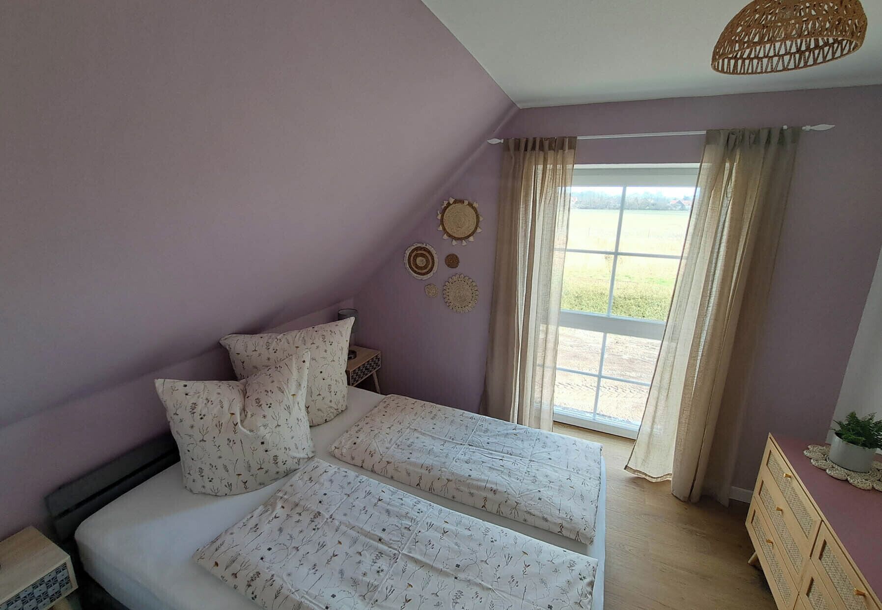 Une chambre à coucher avec un lit, deux tables de chevet, une fenêtre avec des rideaux et un luminaire suspendu.