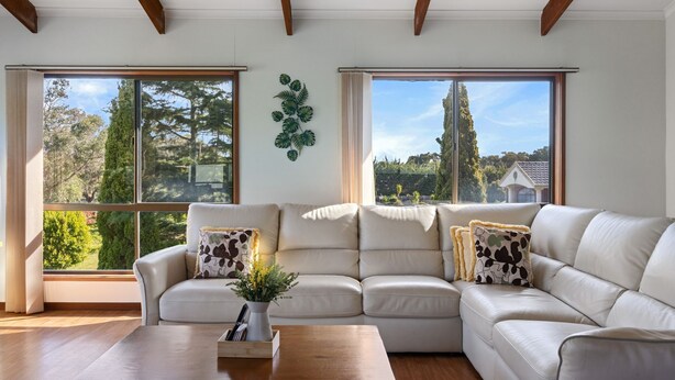 A modern living room with a beige sectional sofa, a wooden coffee table, and large windows offering a view of trees and a house.