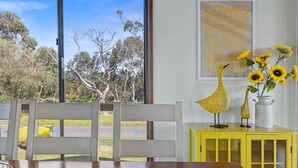 A room with a large window overlooking a garden, a yellow cabinet with decorative items, and a poster on the wall listing various locations.