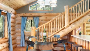 Ein rustikales Blockhaus-Interieur mit einer Holztreppe, einem runden Barbereich mit Hockern und einer Weinflasche.