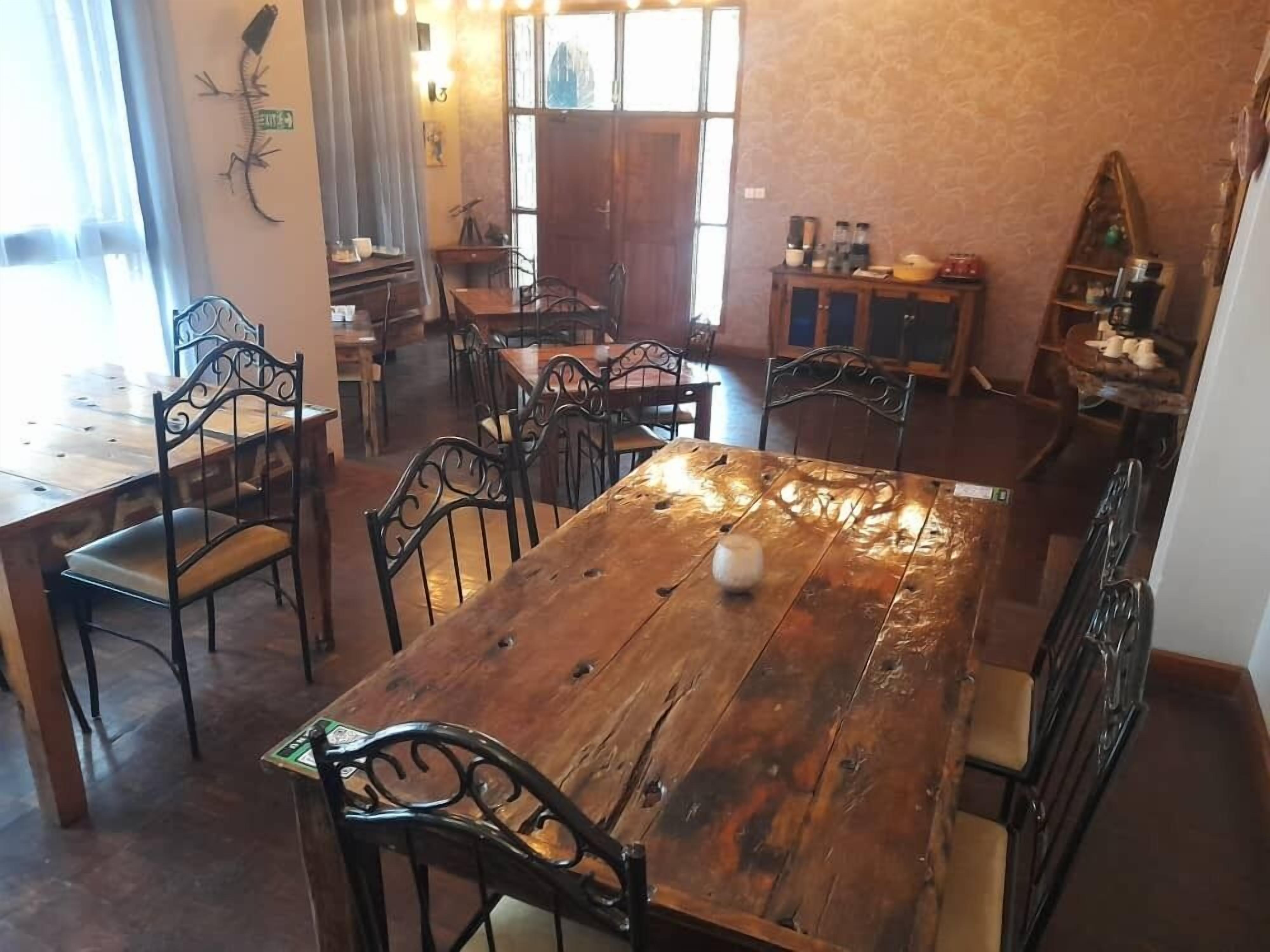 Zona pranzo con tavoli e sedie in legno, angolo cottura con pensili ed elettrodomestici, e vista sulla strada.